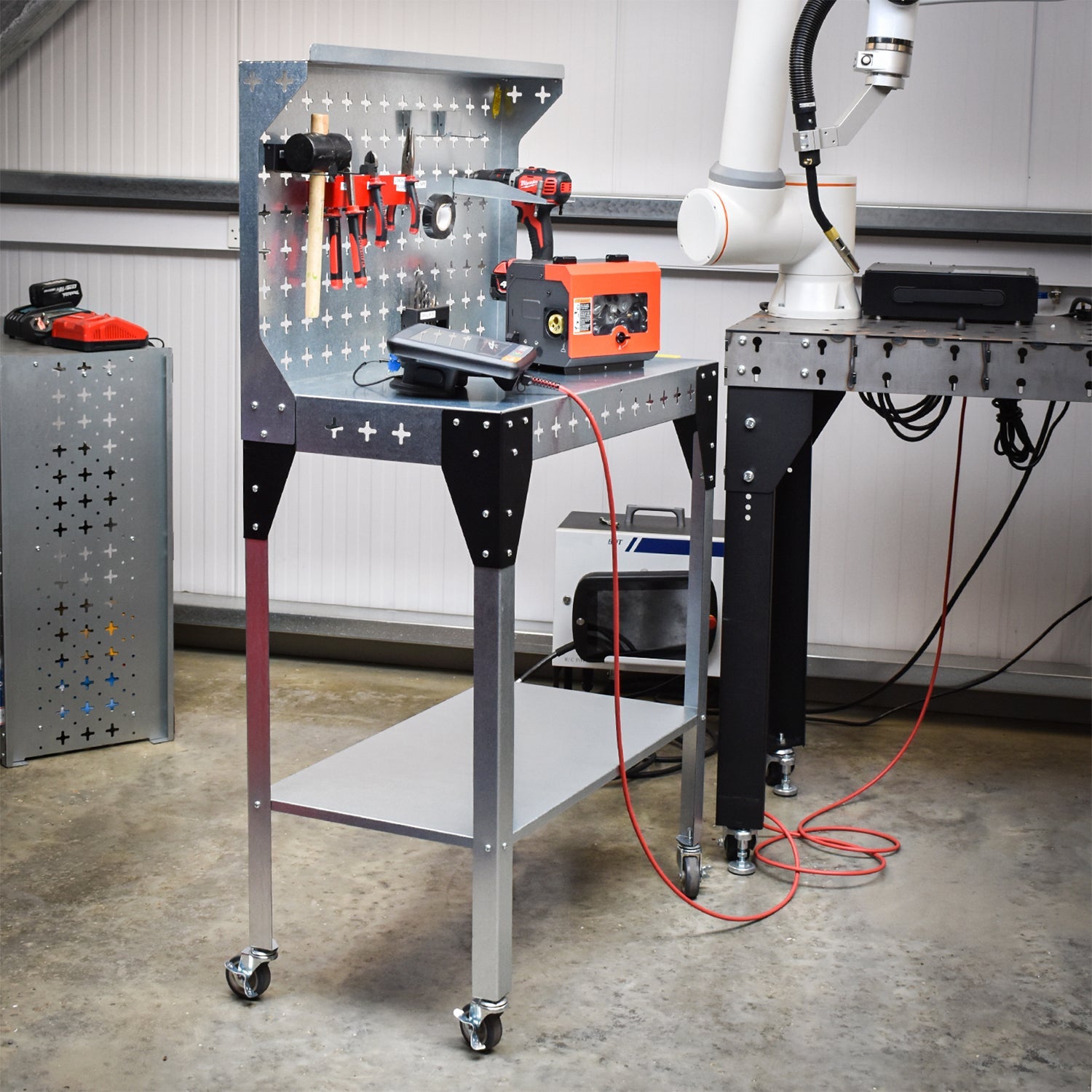 Nukeson Industrial Trolley & Workbench in a Workshop Setting next to a welding robot with equipment stored on the table and the back wall.