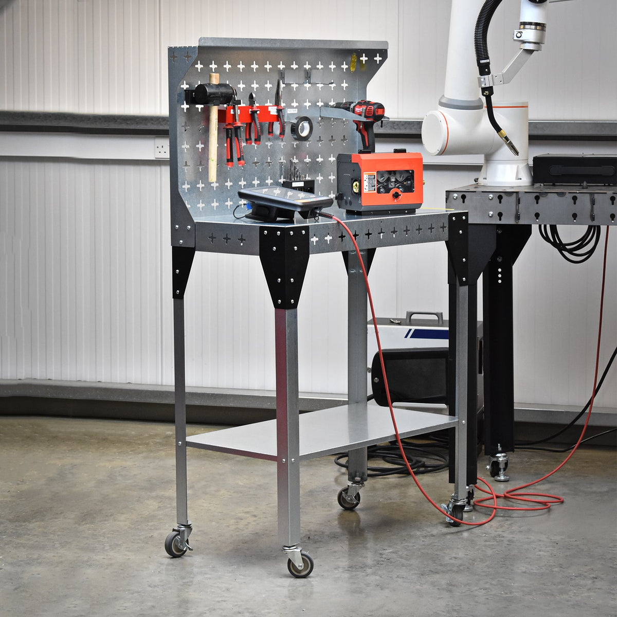 Nukeson Industrial Trolley & Workbench in a Workshop Setting next to a welding robot with equipment stored on the table and the back wall.